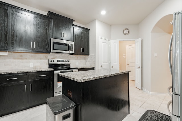3204 Sunny Hill Way, Royse City, TX 75189 - kitchen with appliances with stainless steel finishes, dark cabinetry, a center island, decorative backsplash, and arched walkways