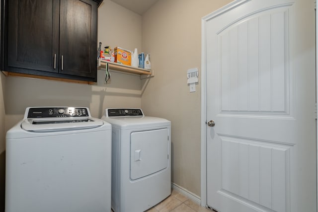 clothes washing area featuring cabinets, light tile patterned flooring, and washing machine and clothes dryer