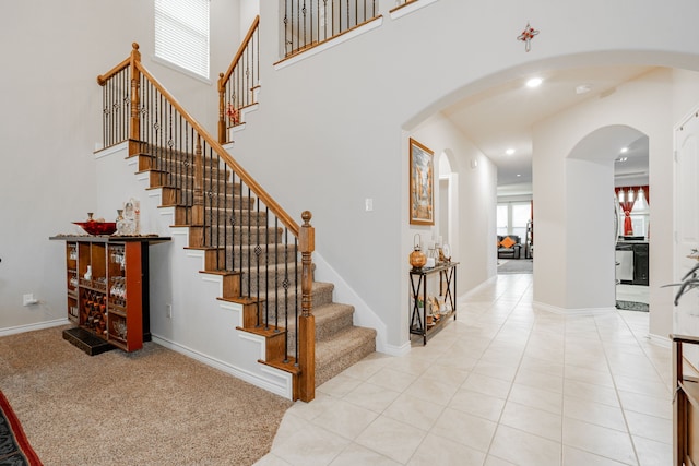 staircase with tile patterned flooring, a healthy amount of sunlight, and a towering ceiling