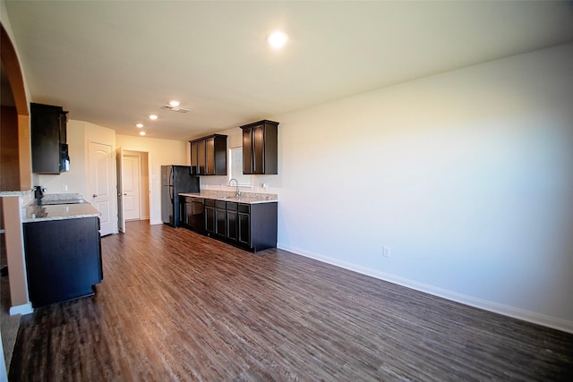 kitchen with light stone countertops, sink, dark hardwood / wood-style floors, dark brown cabinets, and black appliances