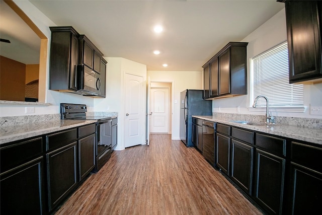 kitchen featuring black appliances, light stone counters, wood-type flooring, and sink