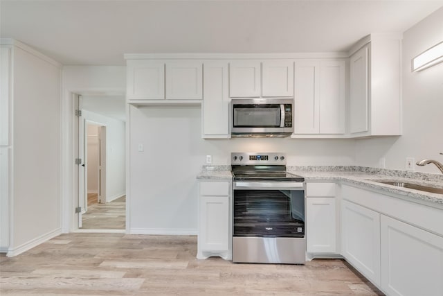 kitchen with white cabinets, appliances with stainless steel finishes, light stone counters, and sink