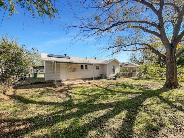 back of property with a lawn, central AC unit, and solar panels