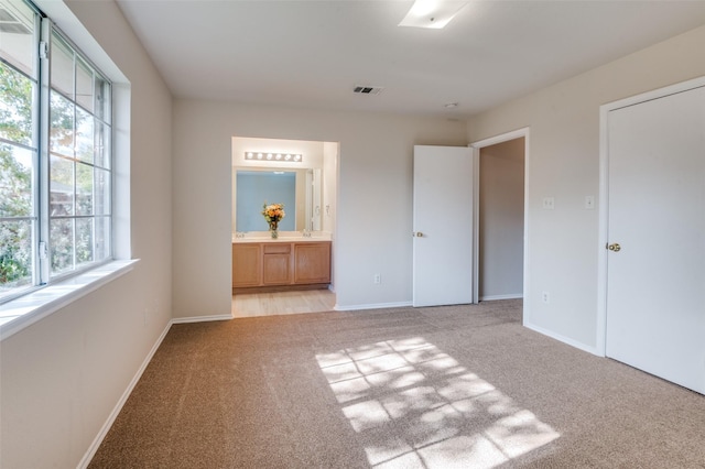 unfurnished bedroom featuring connected bathroom, multiple windows, and light colored carpet