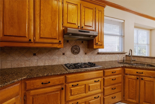 kitchen featuring tasteful backsplash, ornamental molding, dark stone counters, stainless steel gas cooktop, and sink