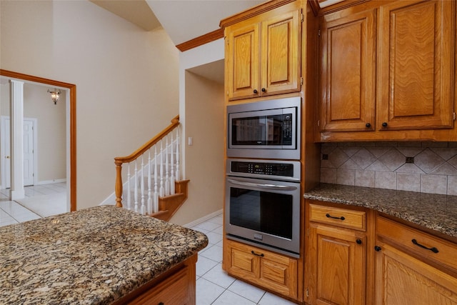 kitchen with appliances with stainless steel finishes, backsplash, light tile patterned floors, and dark stone counters