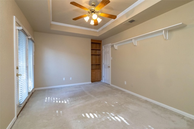 unfurnished bedroom featuring ceiling fan, ornamental molding, light carpet, and a tray ceiling