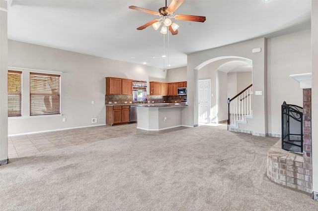 unfurnished living room featuring light colored carpet, a brick fireplace, and ceiling fan