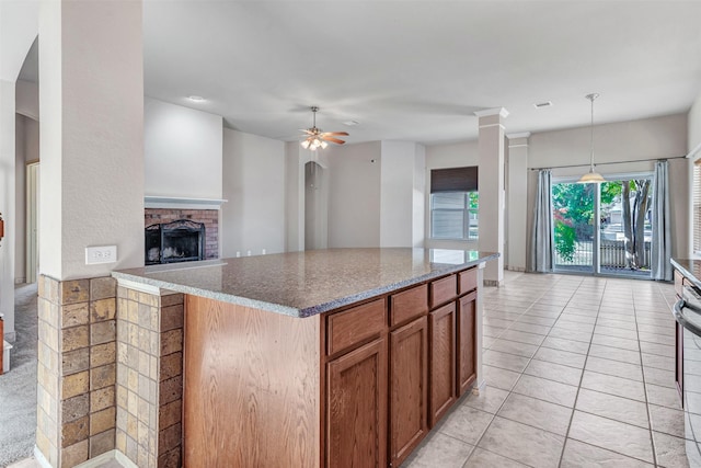 kitchen featuring decorative light fixtures, ceiling fan, light tile patterned floors, a fireplace, and stone countertops