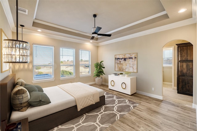 bedroom featuring a raised ceiling, multiple windows, ceiling fan, and light wood-type flooring