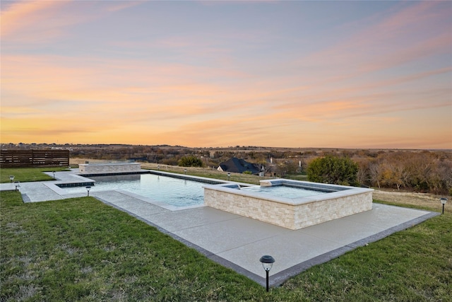 pool at dusk with an in ground hot tub and a yard