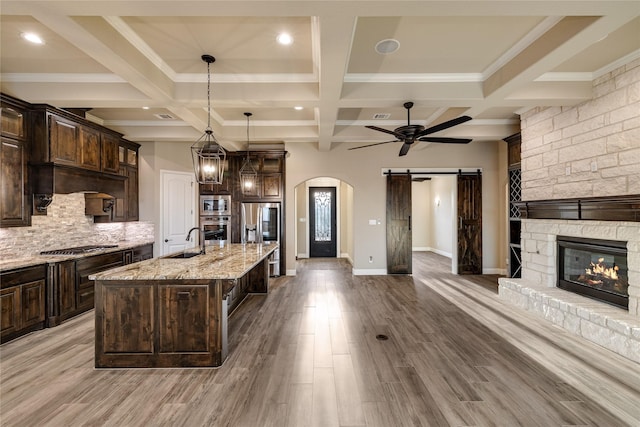 kitchen featuring dark brown cabinetry, stainless steel appliances, a kitchen island with sink, pendant lighting, and hardwood / wood-style flooring