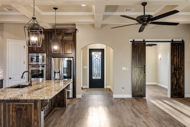 kitchen with light stone countertops, stainless steel appliances, a barn door, hardwood / wood-style floors, and dark brown cabinets