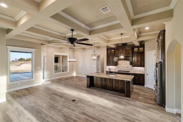 kitchen featuring ceiling fan, light wood-type flooring, an island with sink, tasteful backsplash, and dark brown cabinetry