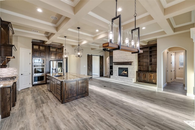 kitchen featuring light stone countertops, stainless steel appliances, pendant lighting, a kitchen island with sink, and light wood-type flooring