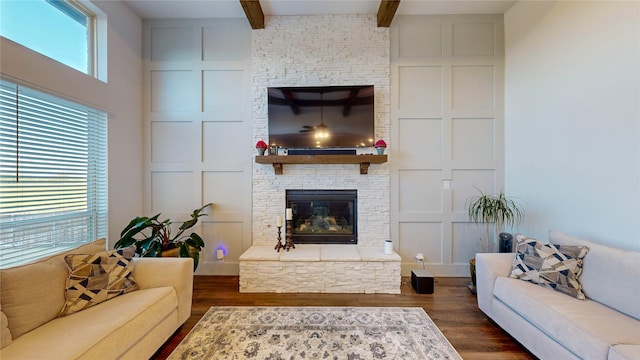 living room featuring beam ceiling, a stone fireplace, dark wood-type flooring, and a wealth of natural light