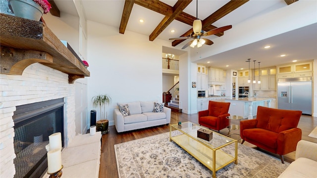 living room with beamed ceiling, ceiling fan with notable chandelier, a fireplace, and dark wood-type flooring