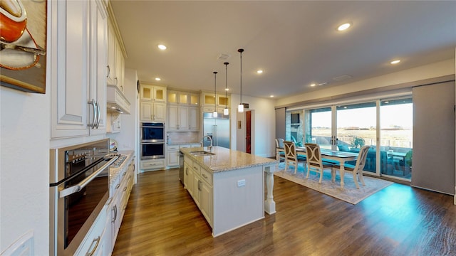 kitchen with light stone counters, dark hardwood / wood-style floors, decorative light fixtures, a kitchen island with sink, and appliances with stainless steel finishes