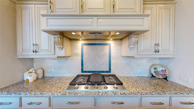 kitchen featuring stainless steel gas stovetop, light stone countertops, backsplash, and custom range hood