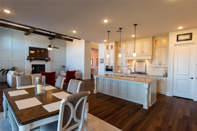 kitchen featuring light stone counters, dark wood-type flooring, an island with sink, and pendant lighting