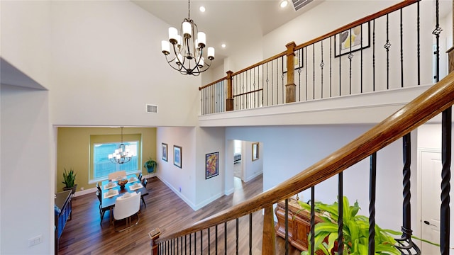 stairway with hardwood / wood-style floors, a high ceiling, and an inviting chandelier