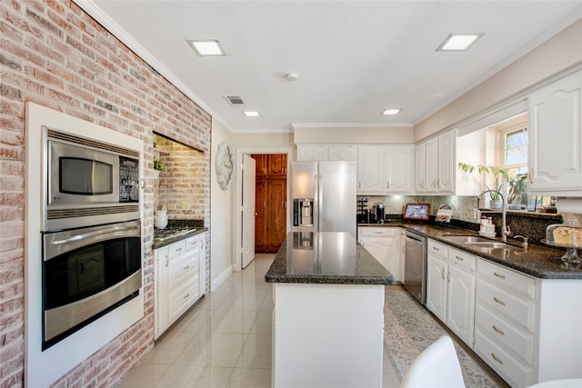 kitchen with a center island, white cabinets, brick wall, light tile patterned flooring, and appliances with stainless steel finishes