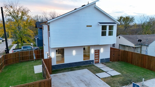 back house at dusk with a lawn and a patio