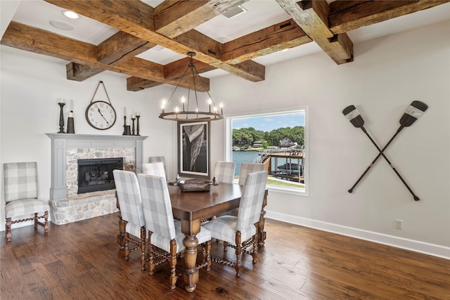 dining space featuring beam ceiling, a stone fireplace, dark wood-type flooring, and an inviting chandelier