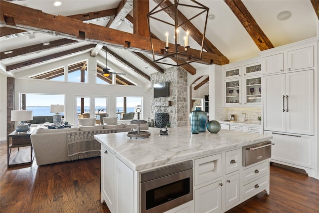 kitchen featuring stainless steel microwave, white cabinetry, a center island, and beamed ceiling