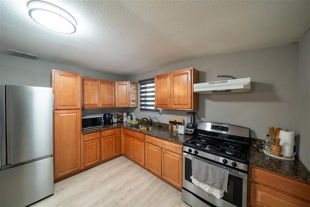 kitchen with sink, a textured ceiling, range hood, appliances with stainless steel finishes, and light hardwood / wood-style floors