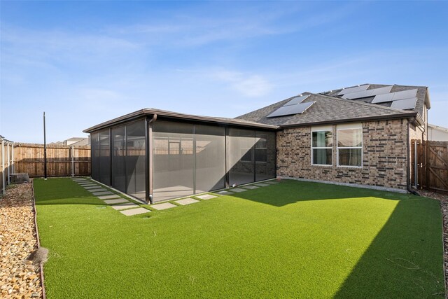 back of property featuring a lawn, a sunroom, and solar panels