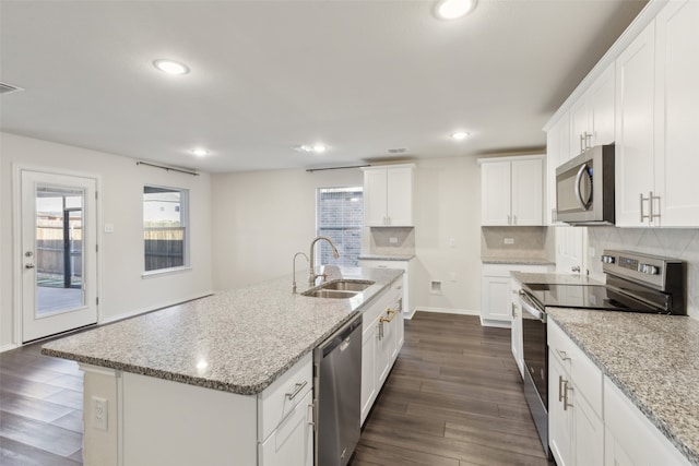 kitchen with a kitchen island with sink, light stone countertops, white cabinets, and appliances with stainless steel finishes