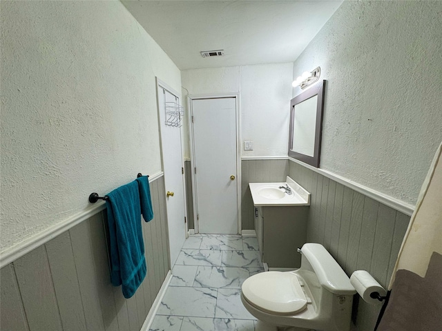 bathroom with vanity, wood walls, and toilet