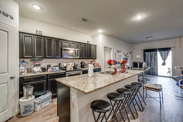 kitchen featuring a breakfast bar area, appliances with stainless steel finishes, light hardwood / wood-style flooring, and an island with sink