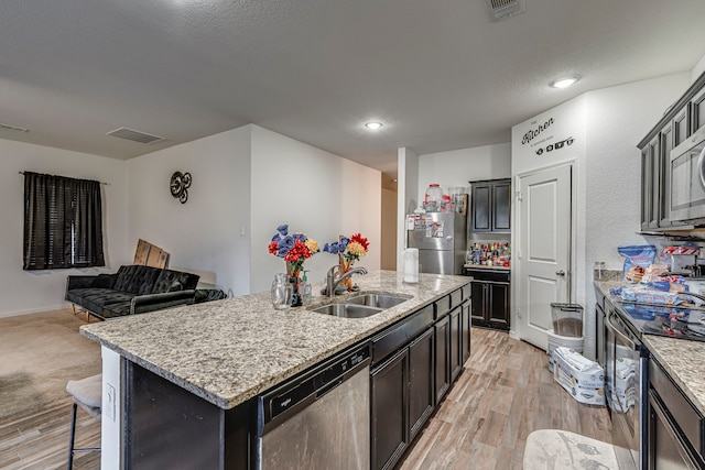 kitchen featuring sink, light wood-type flooring, light stone countertops, an island with sink, and appliances with stainless steel finishes