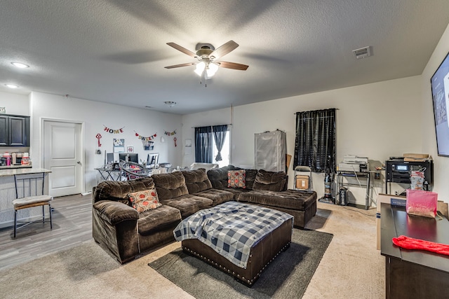 carpeted living room featuring ceiling fan and a textured ceiling