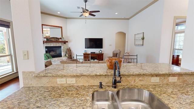 kitchen with light stone counters, a fireplace, crown molding, and sink