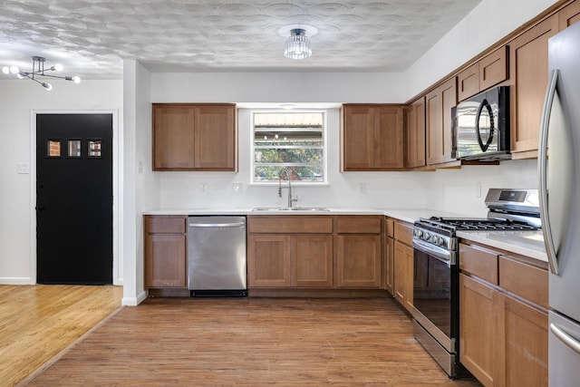 kitchen with appliances with stainless steel finishes, a textured ceiling, sink, light hardwood / wood-style flooring, and a chandelier