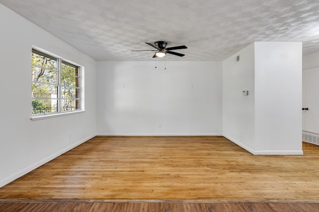 unfurnished room with a textured ceiling, light wood-type flooring, and ceiling fan