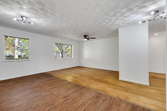 unfurnished room featuring ceiling fan with notable chandelier, a healthy amount of sunlight, wood-type flooring, and a textured ceiling