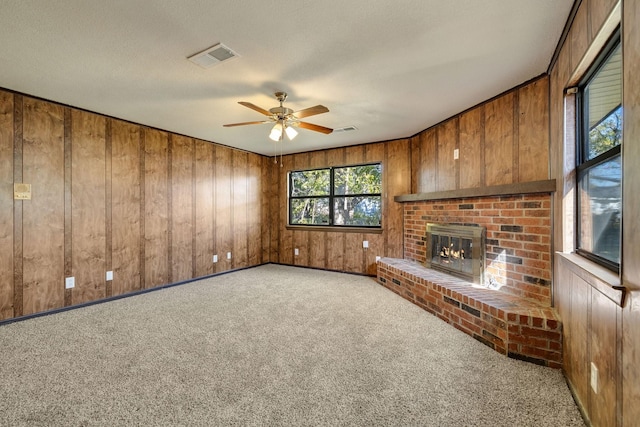 unfurnished living room with light carpet, ceiling fan, wood walls, and a brick fireplace