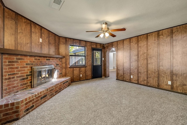 unfurnished living room with light colored carpet, a brick fireplace, and wood walls