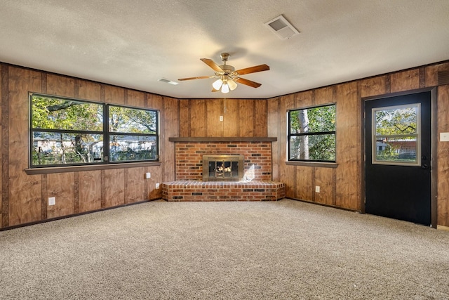 unfurnished living room featuring a fireplace, a textured ceiling, plenty of natural light, and wood walls