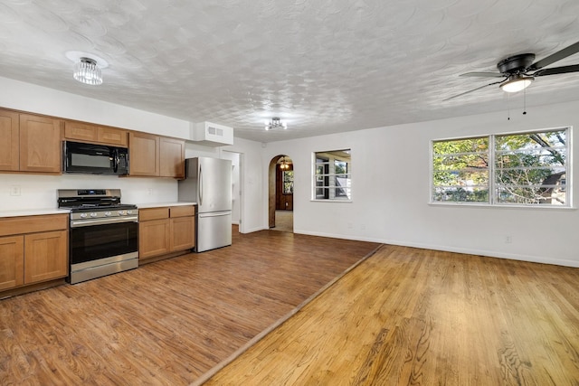 kitchen with ceiling fan, a textured ceiling, appliances with stainless steel finishes, and light hardwood / wood-style flooring