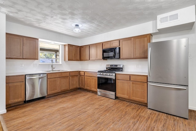 kitchen featuring a textured ceiling, stainless steel appliances, light hardwood / wood-style floors, and sink