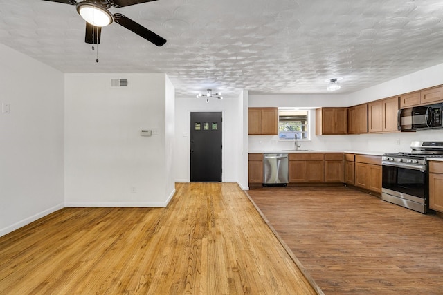 kitchen featuring a textured ceiling, stainless steel appliances, ceiling fan, sink, and light hardwood / wood-style flooring