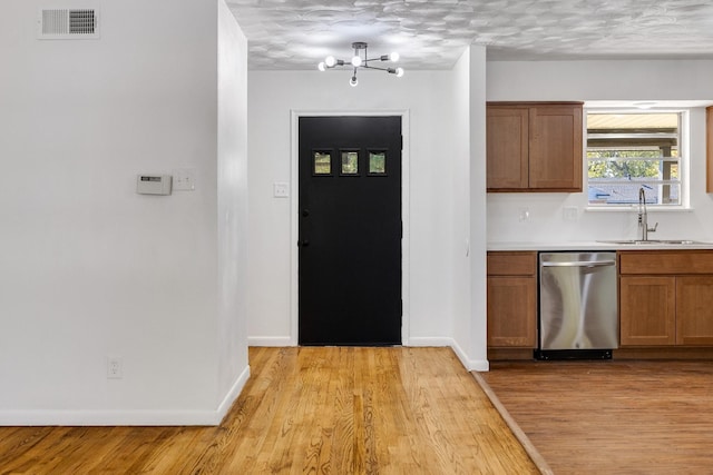 kitchen with dishwasher, sink, a notable chandelier, light hardwood / wood-style floors, and a textured ceiling