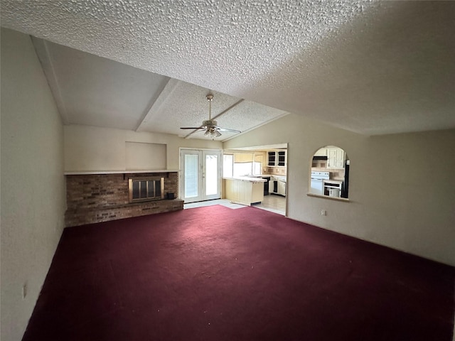 unfurnished living room with vaulted ceiling, ceiling fan, a fireplace, a textured ceiling, and light colored carpet