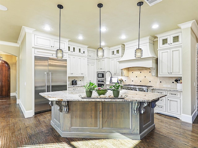 kitchen featuring light stone countertops, dark hardwood / wood-style flooring, built in appliances, decorative light fixtures, and a center island with sink