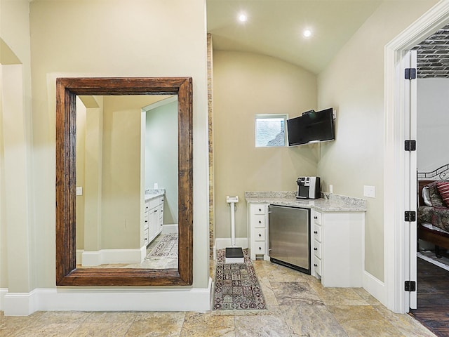 bar featuring light stone countertops, vaulted ceiling, white cabinets, light hardwood / wood-style floors, and stainless steel refrigerator